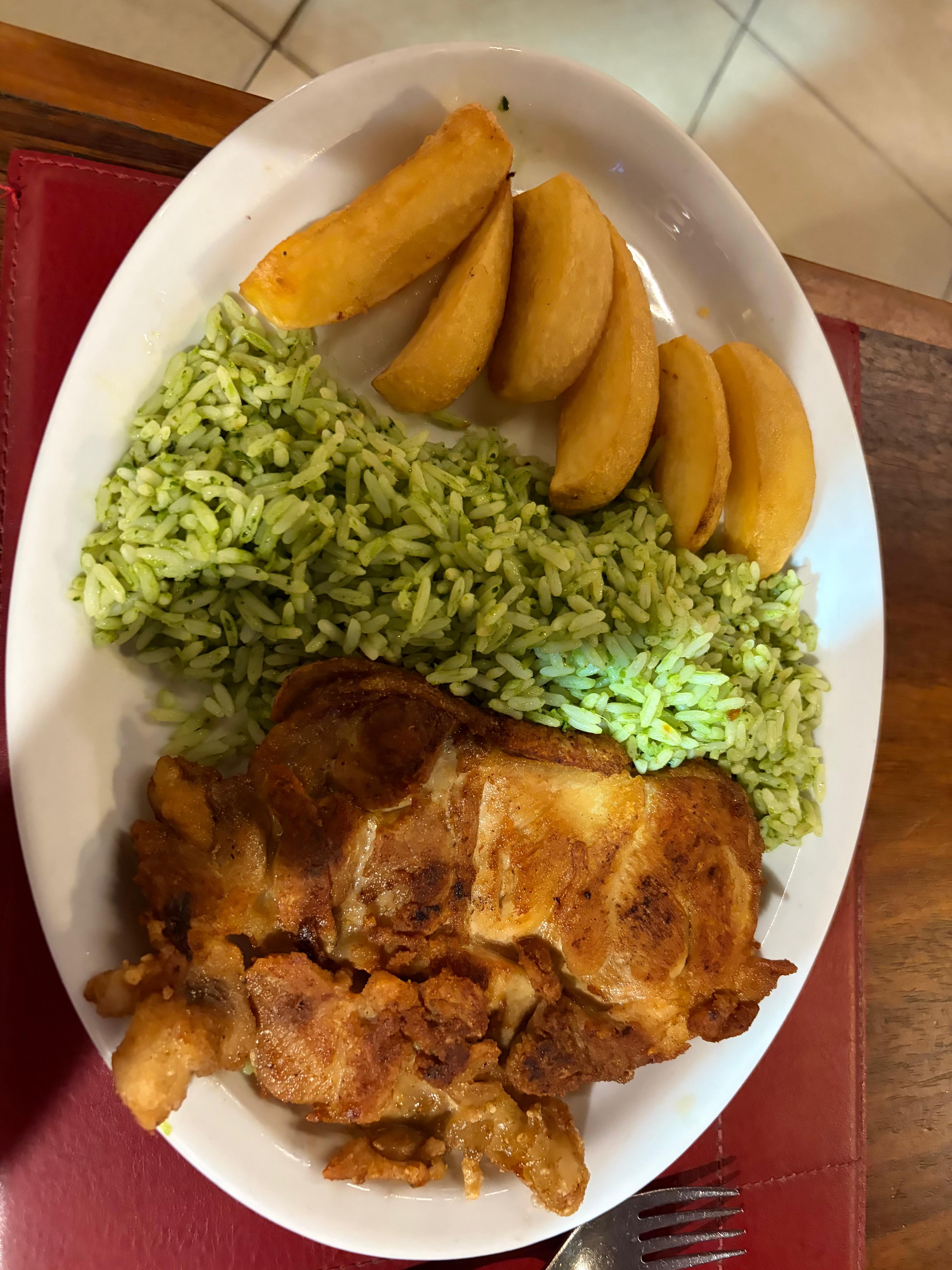 Fried chicken, green rice, and potato wedges.